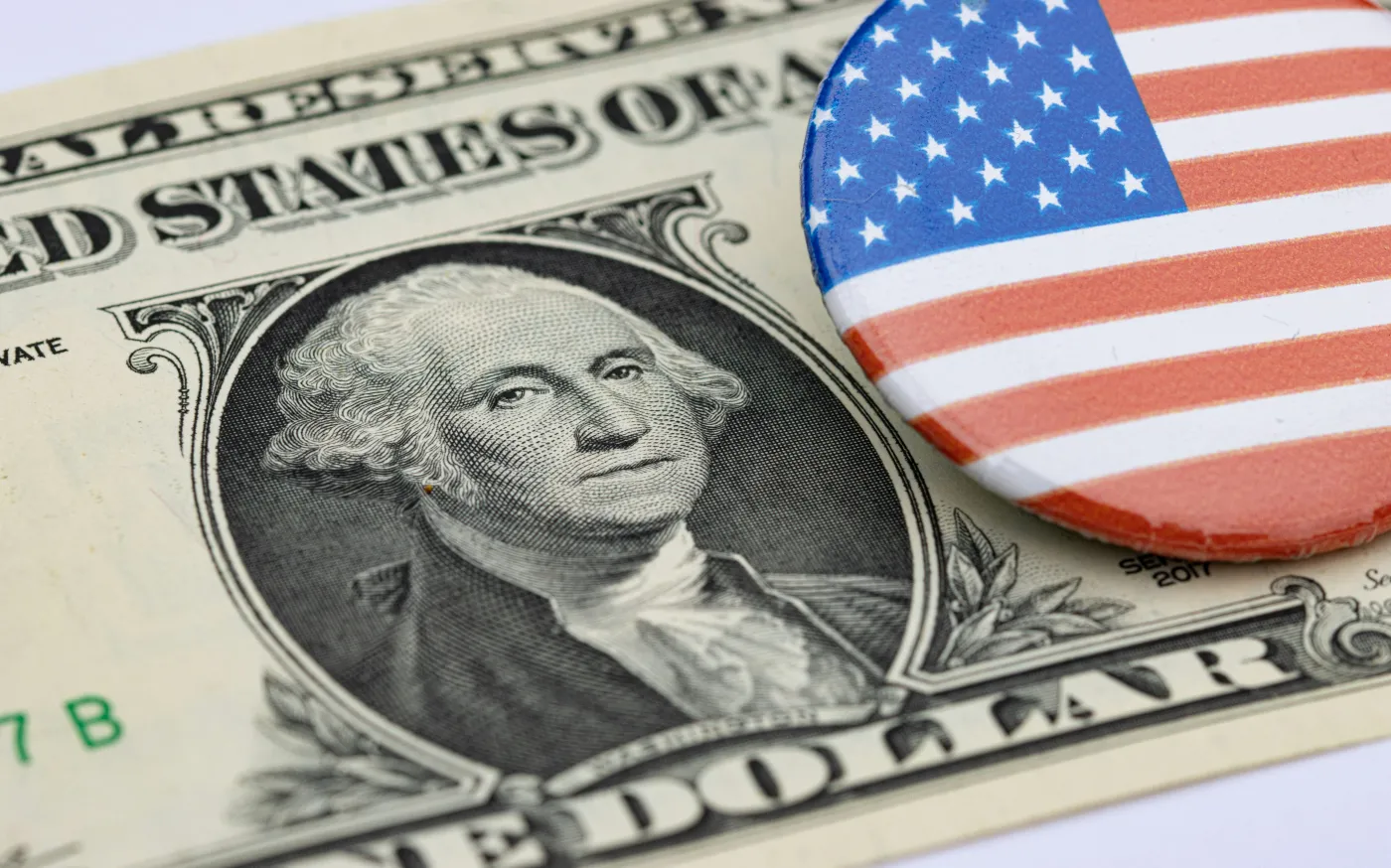 a one dollar bill and a button with the american flag on it by Marek Studzinski courtesy of Unsplash.