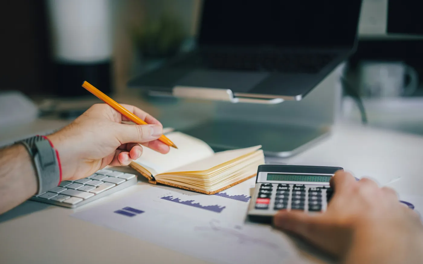 a person sitting at a desk with a calculator and a notebook by Jakub Żerdzicki courtesy of Unsplash.