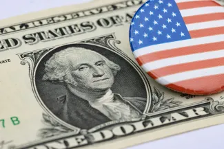 a one dollar bill and a button with the american flag on it by Marek Studzinski courtesy of Unsplash.