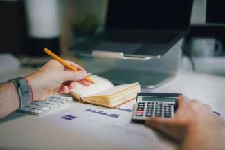 a person sitting at a desk with a calculator and a notebook by Jakub Żerdzicki courtesy of Unsplash.
